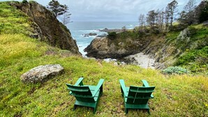 Two green Adirondack chairs facing a rocky coastline with ocean views.