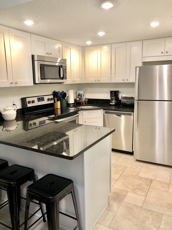 A modern kitchen with white cabinets, stainless steel appliances, a granite countertop, and a central island with stools.