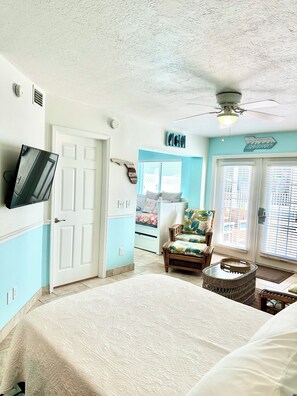 A bedroom with a bed, a chair, a television, and a ceiling fan.