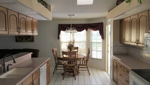 A compact kitchen with wooden cabinets, a dining table with chairs, a built-in oven, and a window with blinds. - Beautiful Home With Heated Pool In A Nice Neighborhood (Spring Hill)