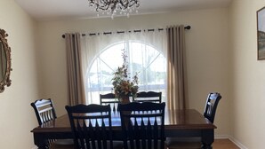 A dining room with a wooden table and chairs, a chandelier, and a window with curtains. - Beautiful Home With Heated Pool In A Nice Neighborhood (Spring Hill)