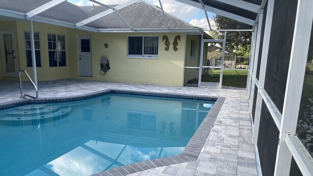 A swimming pool with a tiled deck, a covered area with a roof, and a house in the background. - Beautiful Home With Heated Pool In A Nice Neighborhood (Spring Hill)