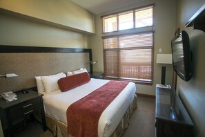 Une chambre d’hôtel avec un lit, un bureau avec un téléphone, une télévision et une fenêtre avec des stores.