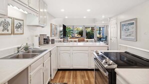 A modern kitchen with white cabinetry, a black stove, and a dining area with a view of the outdoors. - Unit 17, Spacious 2 bedroom Beach Condo with Loft (Panama City Beach)