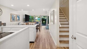 A modern kitchen with white cabinetry, a dining area with a table and chairs, and a staircase leading to another level. - Unit 17, Spacious 2 bedroom Beach Condo with Loft (Panama City Beach)