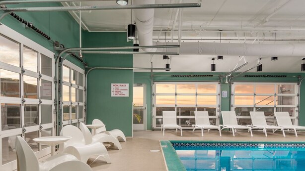 An indoor swimming pool with white lounge chairs and a view of the sunset through the windows. - Modern efficiency unit located on 42nd street, close to beach and convention center! (Ocean City)