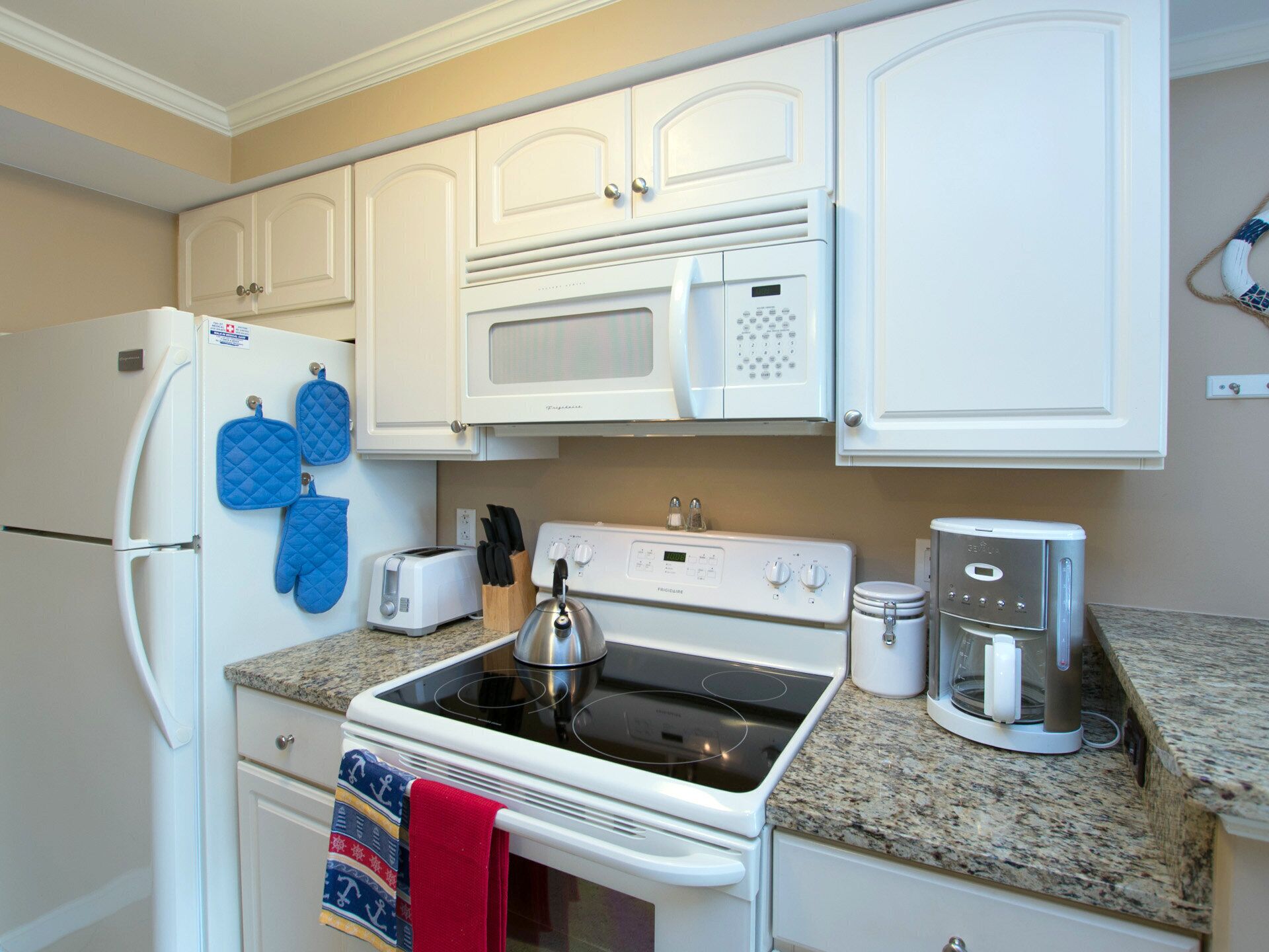A kitchen with white cabinets, a refrigerator, a microwave, a stove, a toaster, and a coffee maker.