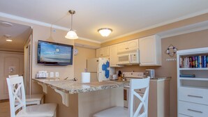 A kitchen with a central island, white cabinetry, a microwave, and a TV displaying 'CENTRAL RESERVATIONS'. - Modern efficiency unit located on 42nd street, close to beach and convention center! (Ocean City)