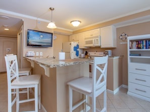 Una cocina con una isla central, armarios blancos, un microondas y un televisor mostrando 'RESERVAS CENTRAL'.
