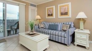 A living room with a striped sofa, a white coffee table, and a side table with a lamp. There are two framed pictures on the wall. - Modern efficiency unit located on 42nd street, close to beach and convention center! (Ocean City)