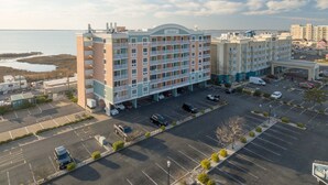 A multi-story hotel with a parking lot in front, a body of water in the background, and a clear sky. - Modern efficiency unit located on 42nd street, close to beach and convention center! (Ocean City)