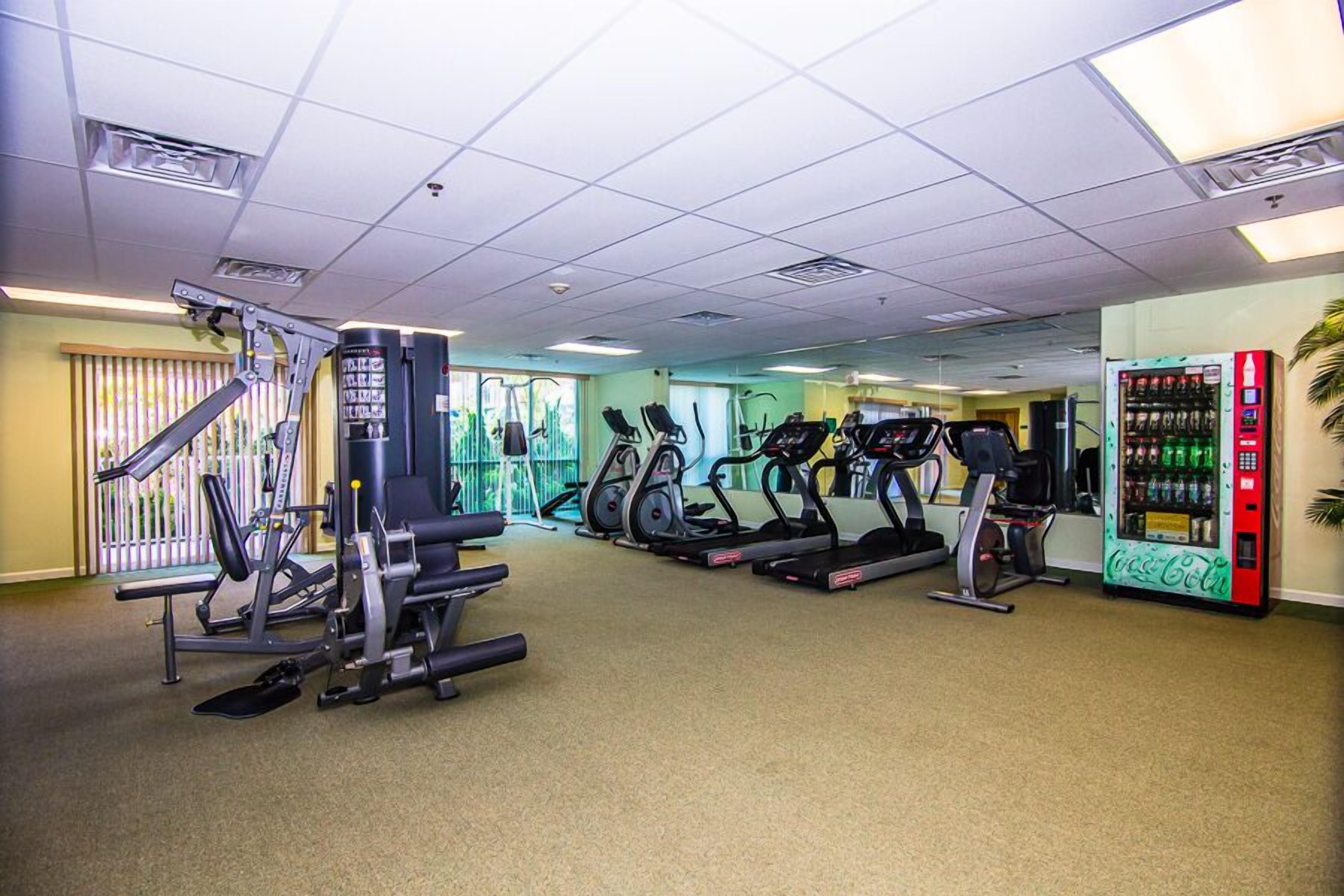 A gym with exercise equipment, a vending machine, and a window with blinds.