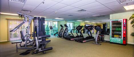 A gym with exercise equipment, a vending machine, and a window with blinds.