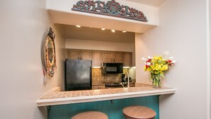 A kitchen with a central island, two stools, a refrigerator, a microwave, and a decorative wall piece. - Beautiful Southwest Style Old Town Scottsdale, Ground Level Condo (Scottsdale)