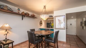 A dining area with a round table, four chairs, a lamp, shelves with decorative items, and a door leading to another room. - Beautiful Southwest Style Old Town Scottsdale, Ground Level Condo (Scottsdale)