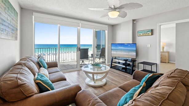 Una sala de estar con sofá, televisor y balcón con vista a la playa.