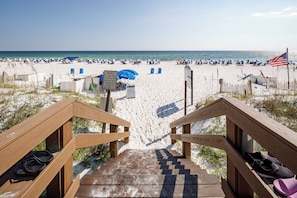 Une plage avec un escalier en bois menant au sable, un panneau avec du texte et un drapeau américain.