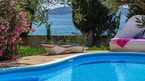 A pool with lounge chairs and a tray of drinks, surrounded by greenery and a view of the sea.