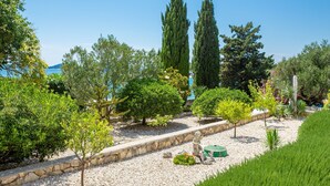 A landscaped garden with various trees, a stone pathway, and a statue.