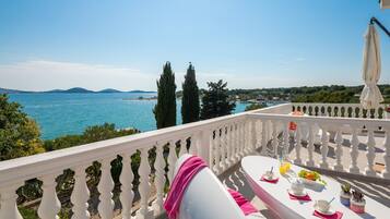 A balcony with a table set for breakfast, overlooking a body of water and distant hills.