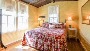 A bedroom with a floral bedspread, two bedside lamps, a ceiling fan, and a window with curtains.