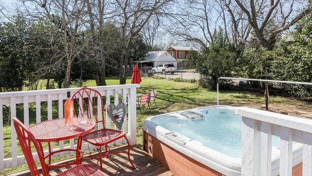 A hot tub on a wooden deck with a white railing, surrounded by trees and a lawn.