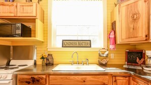 A kitchen with wooden cabinets, a white stove, a sink, and a window with a 'Kindness Matters' sign.