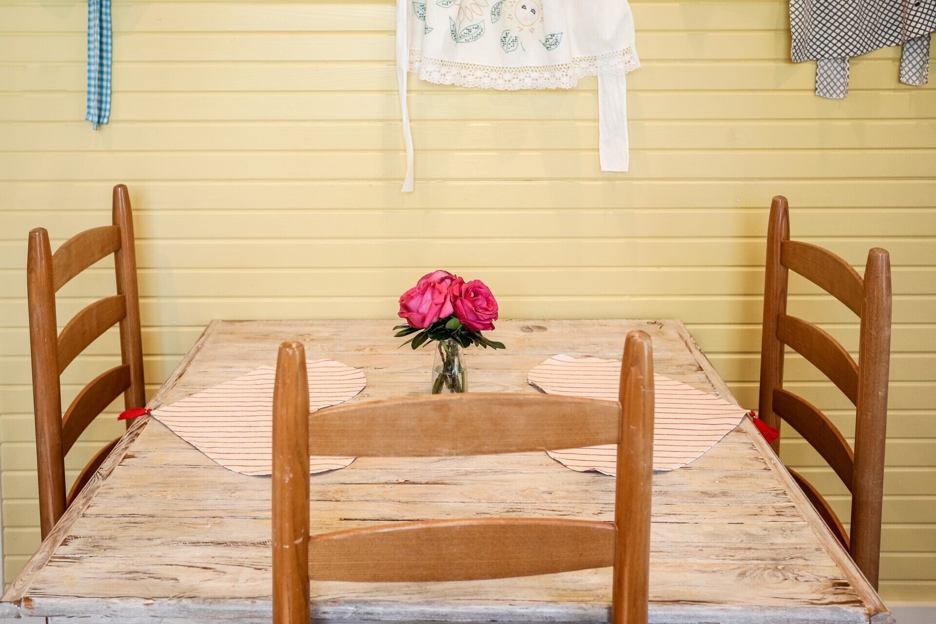Een houten tafel met stoelen, een vaas met roze bloemen en een kantkleed.