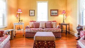 A cozy living room with a floral-patterned sofa, matching ottoman, and two side tables with lamps.
