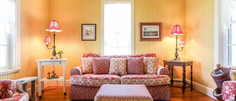 A cozy living room with a floral-patterned sofa, matching ottoman, and two side tables with lamps.