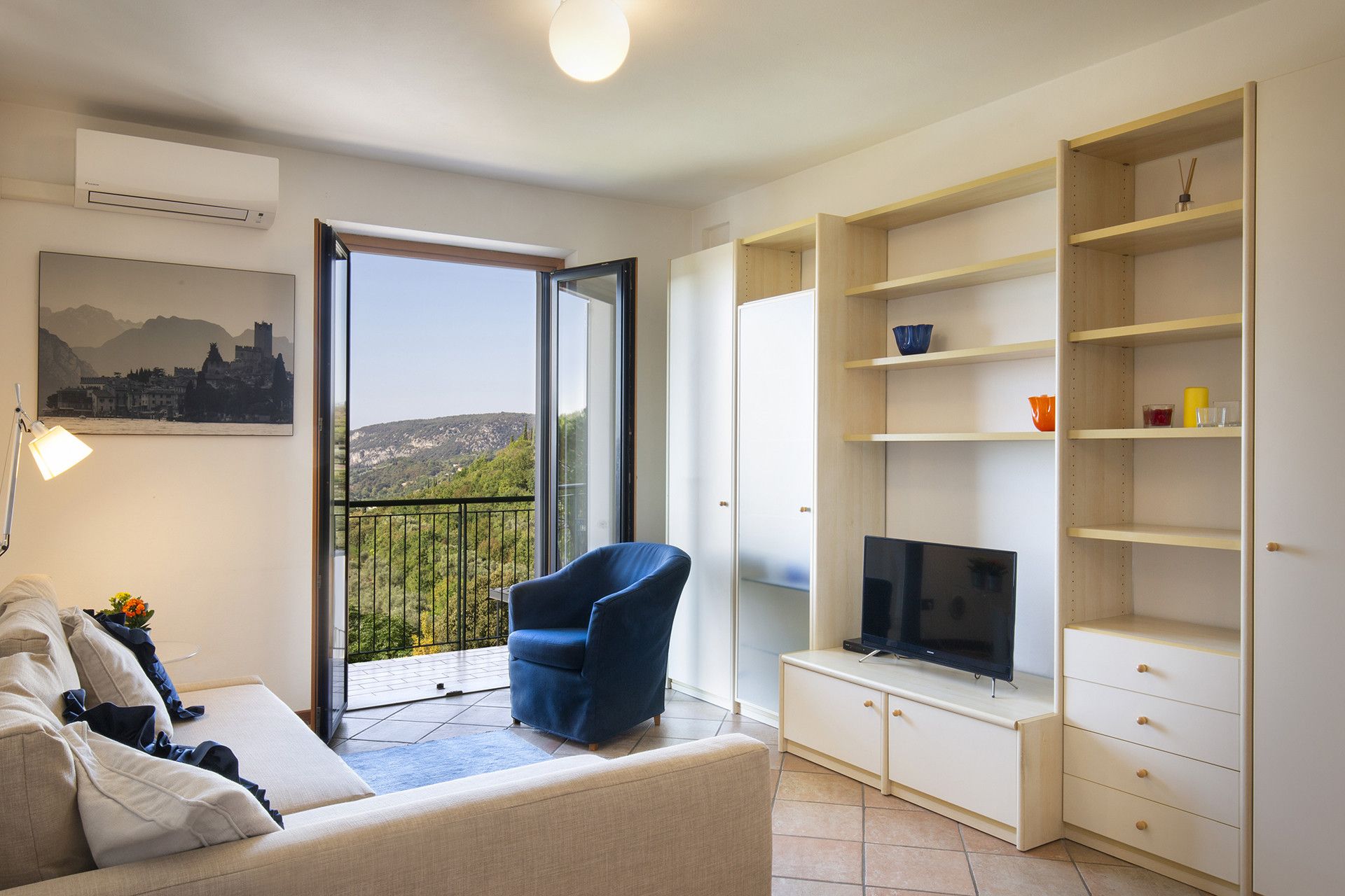 A modern living room with a sofa, a blue armchair, a TV, and a balcony with a cityscape view.