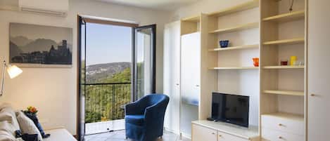 A modern living room with a sofa, a blue armchair, a TV, and a balcony with a cityscape view.