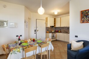 A compact kitchen with a dining area, featuring a table set for two, a blue sofa, and a tiled floor.