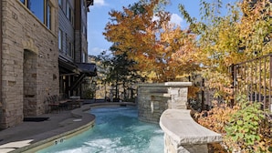 A spa area with a hot tub, stone walls, and a view of a building with large windows.