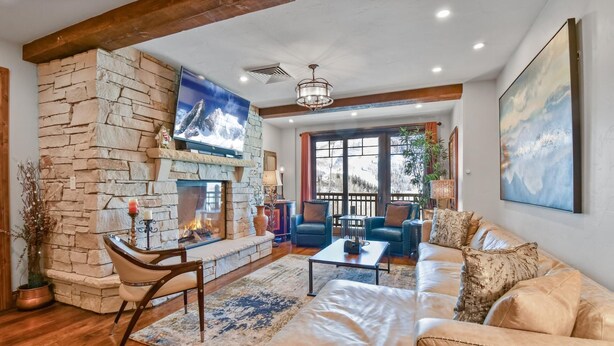 A cozy living room with a stone fireplace, leather sofa, and a television mounted above it.
