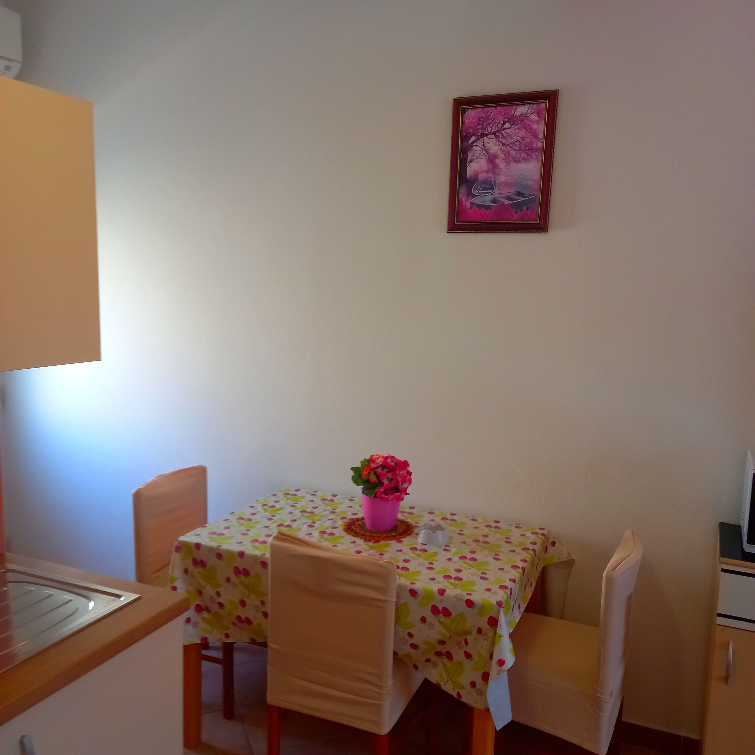 Ein kleiner Essbereich mit einem Tisch, der mit einer blumigen Tischdecke bedeckt ist, zwei Stühlen und einer rosa Blumenvase.