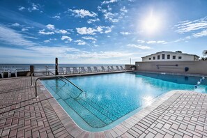 Una piscina con acqua cristallina e blu, circondata da un solarium in mattoni, con vista sull'oceano.