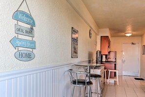 Un corridoio con un cartello che dice 'Welcome to our home', una zona cucina con un frigorifero e un’area pranzo con due sedie e un tavolo.