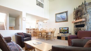 A spacious living room with a high ceiling, a dining area with wooden furniture, a fireplace with a stone surround, and a television on a stand. - W3533 | Vaulted Ceilings | Nice Views | Winter Shuttle | Pool | Hot Tub (Steamboat Springs)