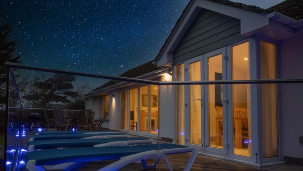 Ein modernes Haus mit Schwimmbad, großen Glasfenstern und einem sternenübersäten Nachthimmel.