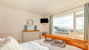 Ein Schlafzimmer mit einem großen Bett, einem Schminktisch, einem Fernseher und einem Fenster mit Blick.