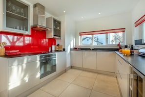 A modern kitchen with a red backsplash, stainless steel appliances, and a large window with a view of the outside.
