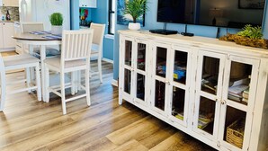 Eine moderne Küche mit weißen Schränken, ein Essbereich mit weißen Stühlen, ein Fernseher auf einem weißen Schrank und ein Schild mit der Aufschrift Florida an der Wand.