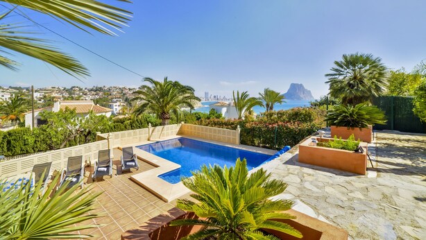 Ein Pool auf dem Dach mit Liegestühlen, Palmen und Blick auf Stadt und Meer.
