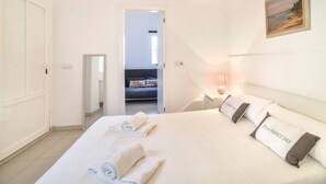 Ein Hotelzimmer mit einem ordentlich bezogenen Bett, einem Bild an der Wand und Blick in das angrenzende Zimmer.