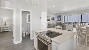 A modern kitchen with an island, a dining area with a table and chairs, a living room with a sofa, and a view of the ocean. - Reserve now. Beautiful pool and ocean. Easy social distancing. Huge pool deck. <br> (Fort Morgan)