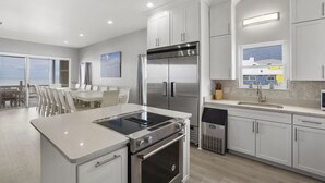 A modern kitchen with stainless steel appliances, a dining area with a view, and a large window. - Reserve now. Beautiful pool and ocean. Easy social distancing. Huge pool deck. <br> (Fort Morgan)