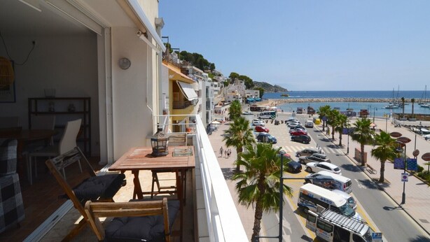 A balcony with a table and chairs, overlooking a busy street with cars and a beach. - ESCORPORA (Estartit)