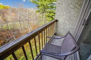 A balcony with a metal chair, a wooden railing, and a view of trees and a building in the background.
