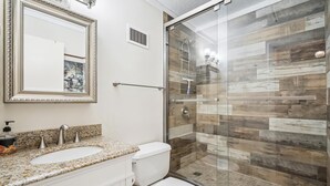 Une salle de bain avec un double lavabo, des toilettes, une douche à parois de verre et un miroir doté d’un cadre décoratif.